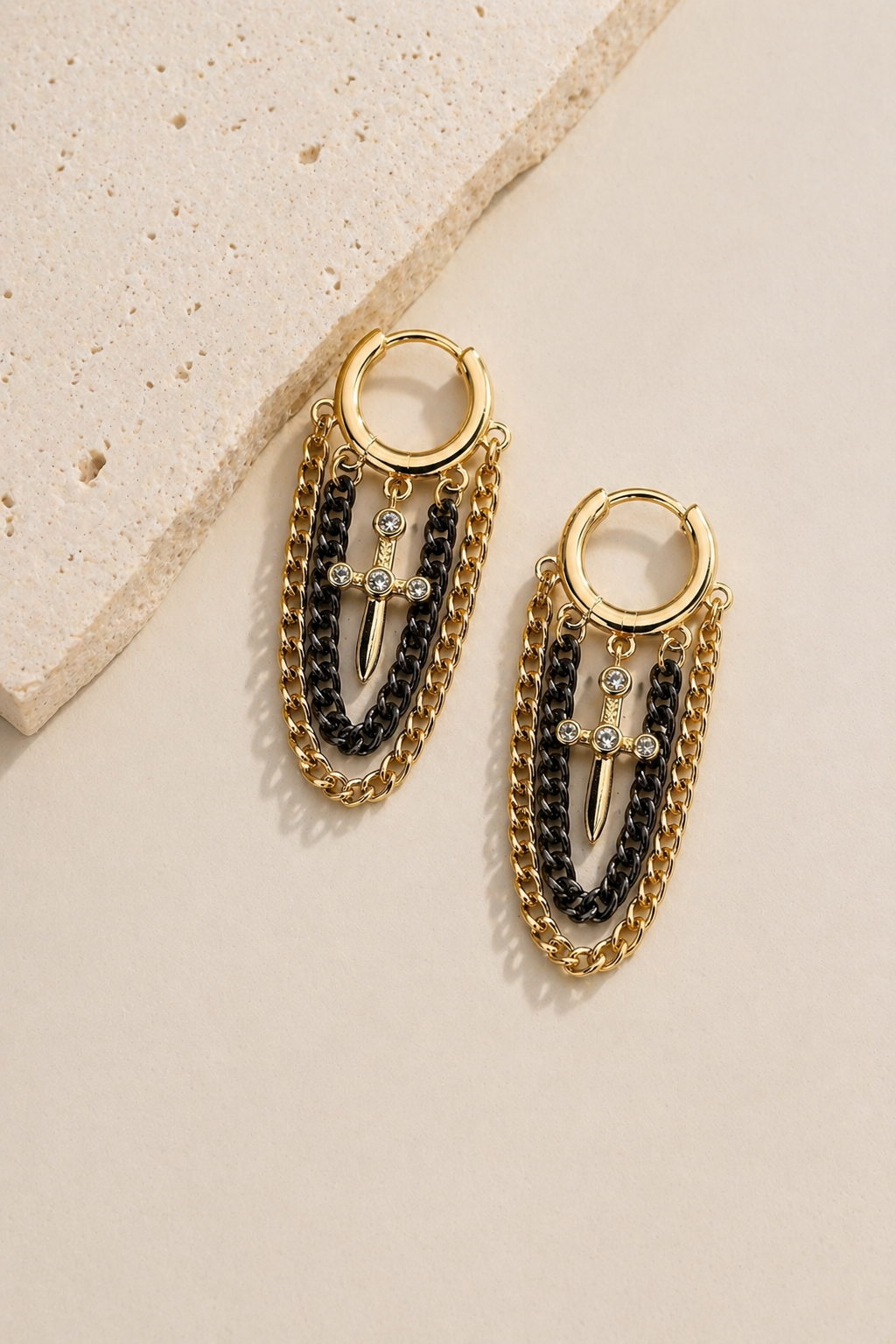 Arracadas tipo huggie con cadenas colgantes en oro y gun metal con dije de daga y microzirconias marca Cianna
