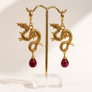 Par de aretes de dragón dorados con gotas de rubí natural facetado sobre un soporte de joyería.