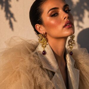 Modelo luciendo aretes de dragón con rubí natural facetado y baño de oro en sesión de fotos de moda editorial.