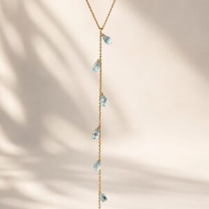 Modelo luciendo un elegante collar de topacio azul natural tipo corbata en chapa de oro de 22k sobre un escote pronunciado.